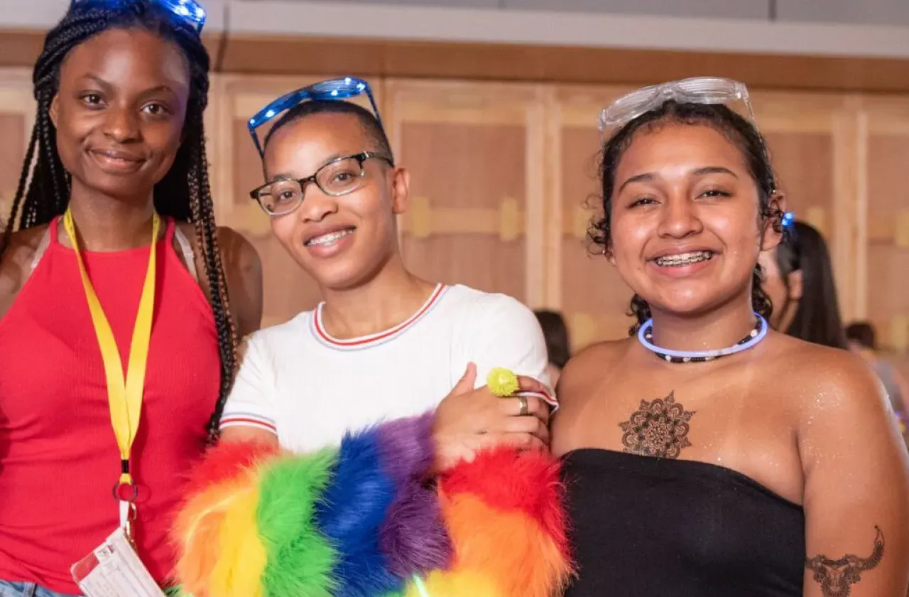 Three WGR students, smiling at the camera with glow-stick necklaces and glasses on.